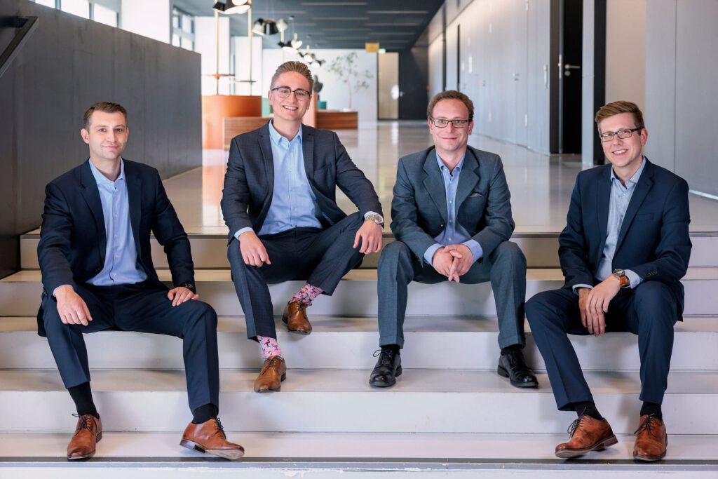 Das vierköpfige Team der plasmotion GmbH sitzend auf der Treppe. Ganz links Michael Penzel (Produktion & Entwicklung), gefolgt von Geschäftsführer Vincent Stepputat, danach Justus Brenger (Finanzen & Einkauf) und ganz rechts Sam Schröder (Technologie & Qualität)