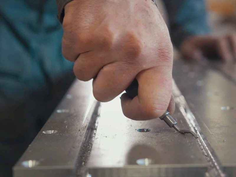 Male hands makes chamfering removing burrs on metal panel with a scraper, close up