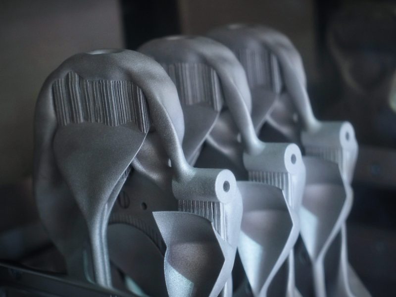 three complex shaped additively manufactured, 3d printed metal parts in powder bed showing support structures